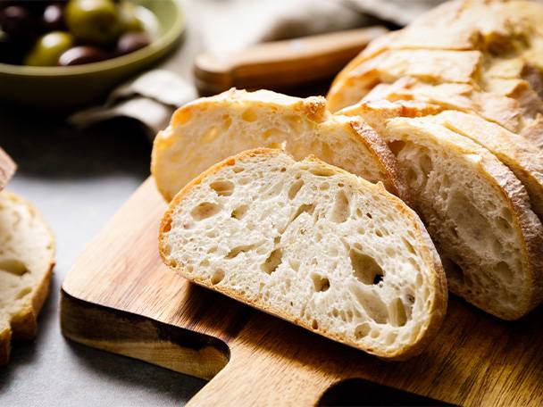 Ein Holzbrett mit frisch geschnittenem Weißbrot und einer Schale Oliven im Hintergrund.