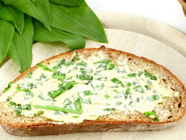 Ein Stück Brot mit Kräuterbutter und frischem Bärlauch auf einem Holzbrett.