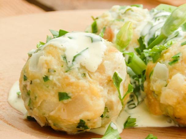 Knödel mit cremiger Soße und frischen Kräutern auf einem Holzteller.