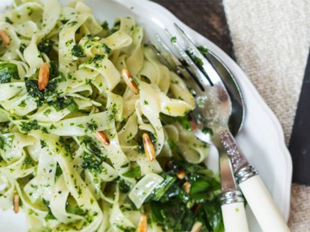 Fettuccine-Nudeln mit Pesto, Pinienkernen und grünem Gemüse auf einem weißen Teller.
