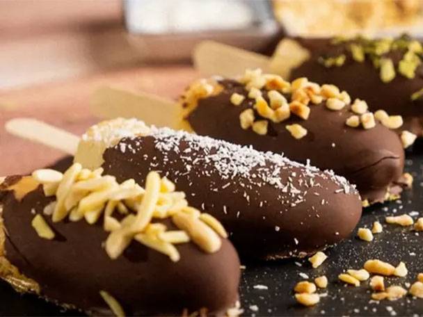 Schokoladenüberzogene Bananen-Pops mit verschiedenen Nüssen und Kokosraspeln