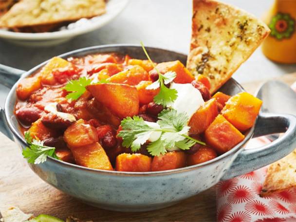 Eine Schüssel mit Kürbis-Chili, garniert mit Sauerrahm und Koriander, dazu ein Stück Fladenbrot.