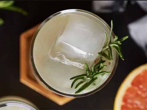 Ein Glas mit einem Getränk, Eiswürfel und Rosmarin, von oben gesehen.
