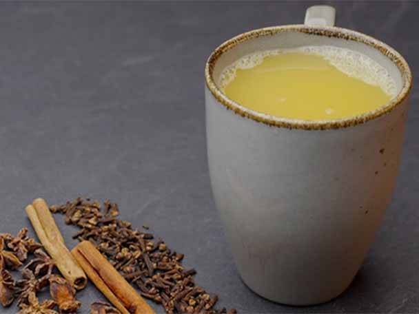 Ein Becher mit gelbem Getränk und Gewürzen wie Zimtstangen und Nelken.
