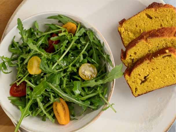 Ein Teller mit Rucolasalat und Kirschtomaten neben Scheiben von gelbem Brot.