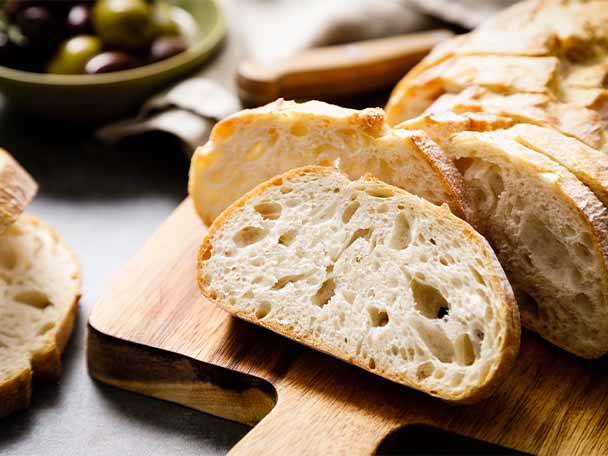 Geschnittenes Brot auf einem Holzbrett mit Oliven im Hintergrund.