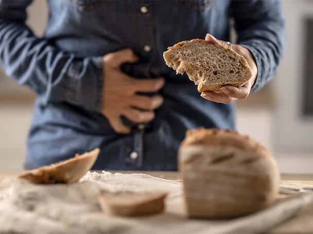 Eine Person hält ein Stück Brot und hält sich den Bauch, während Brot auf dem Tisch liegt.