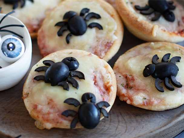 Halloween-Pizzen mit Oliven-Spinnen und einem gruseligen Augapfel in einer Schale.