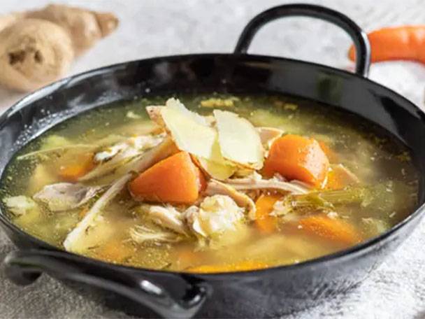 Hühnersuppe mit Karotten, Sellerie und Ingwer in einer schwarzen Schüssel