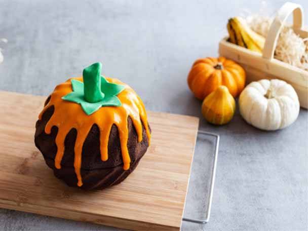 Kürbiskuchen mit orangefarbenem Zuckerguss und Kürbissen auf einem Schneidebrett.