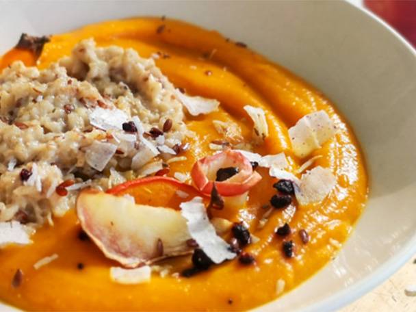Eine Schüssel mit orangefarbenem Püree, Haferflocken, Kokosflocken, Beeren und Apfelscheiben.