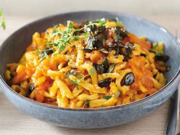 Schupfnudeln mit Kürbis-Tomaten-Soße, Kürbiskernen und frischen Kräutern in einer blauen Schale