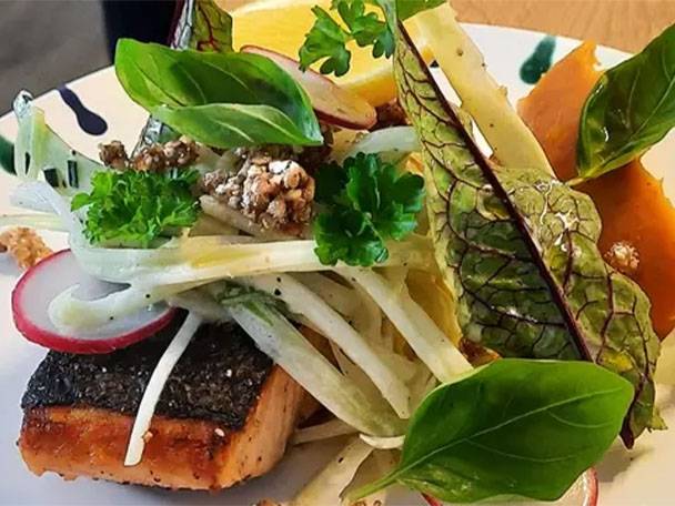 Lachsfilet mit Fenchelsalat, Radieschen, Kräutern und Kürbis auf einem Teller.