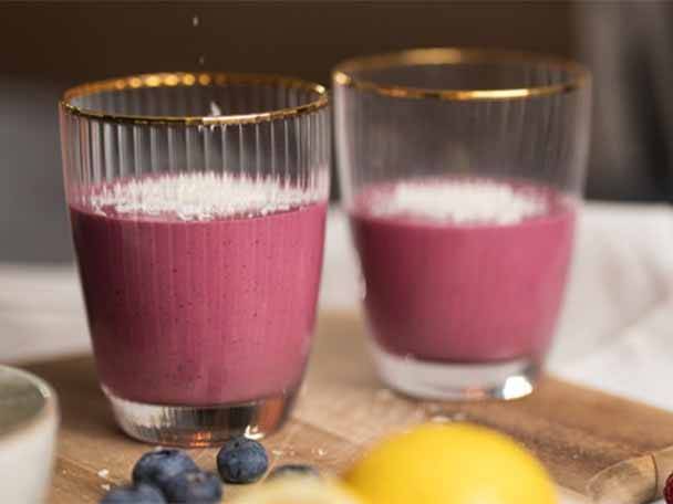 Zwei Gläser mit pinkem Smoothie, bestreut mit Kokosflocken, auf einem Holzbrett.