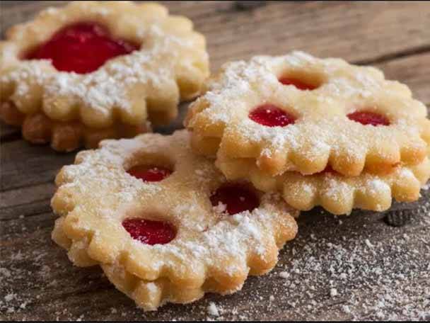 Zwei Reihen von Plätzchen mit roter Marmeladenfüllung und Puderzucker auf einem Holztisch.