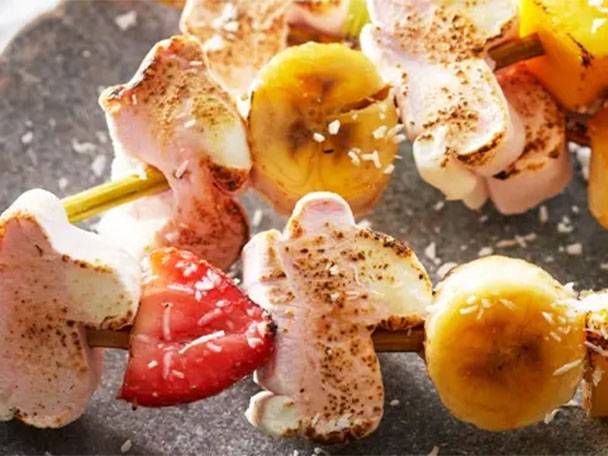 Gegrillte Marshmallow- und Fruchtspieße mit Banane, Erdbeere und Kokosraspeln.