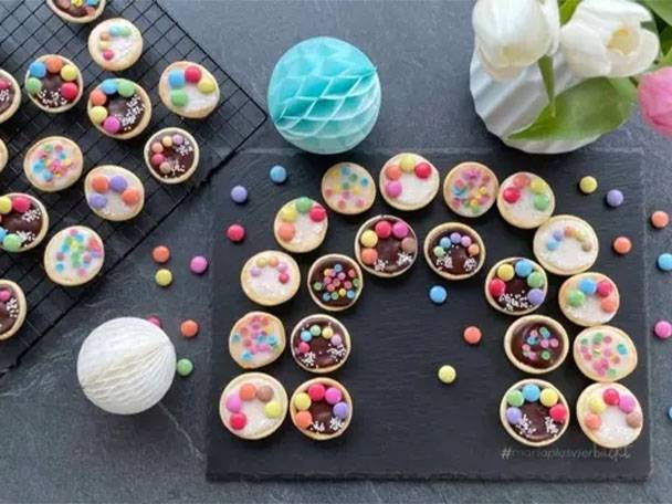 Bunte Kekse mit Schokolade und Zuckerstreuseln auf schwarzem Hintergrund