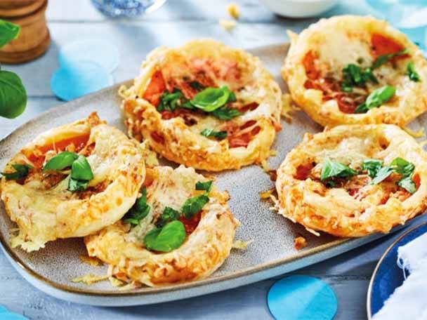 Eine Platte mit herzhaften Törtchen, gefüllt mit Tomaten, Käse und Basilikum.