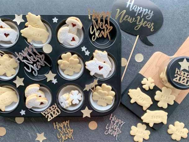 Neujahrs-Glückskekse in Schweine- und Kleeblattform in einer Muffinform und auf einem Holzbrett.