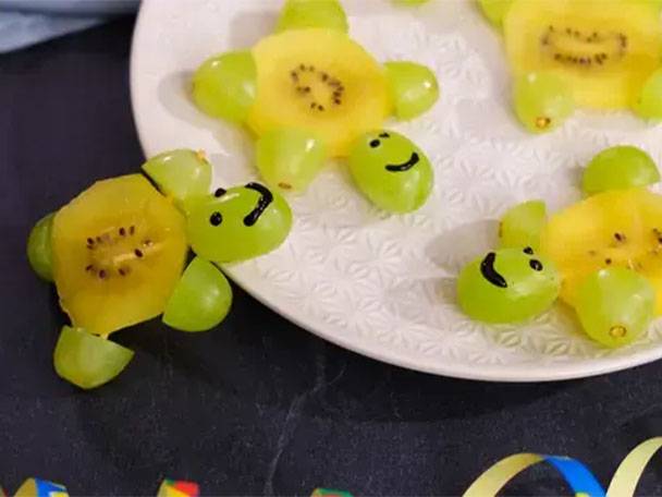 Schildkröten aus Kiwi und Weintrauben auf einem weißen Teller