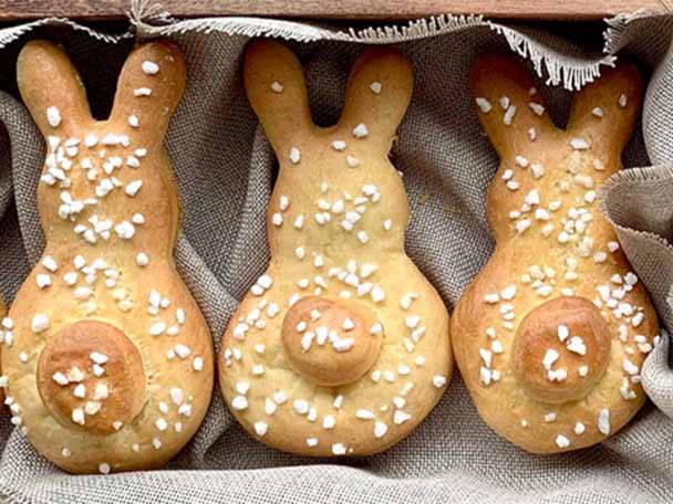 Drei hasenförmige Brötchen mit Zuckerstreuseln in einer Holzkiste.