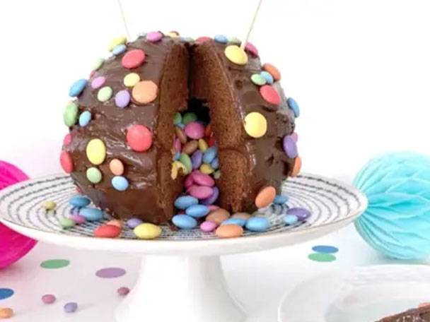 Schokoladenkuchen mit bunten Smarties und Überraschungsfüllung auf einer Tortenplatte.