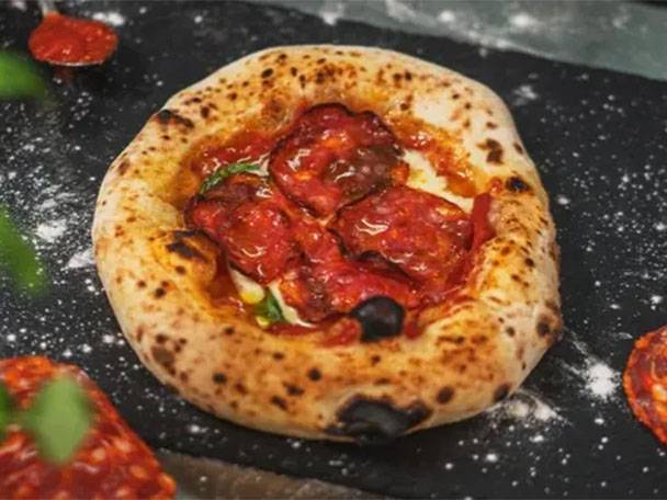 Eine kleine, runde Pizza mit roter Soße und Belag auf schwarzem Hintergrund.