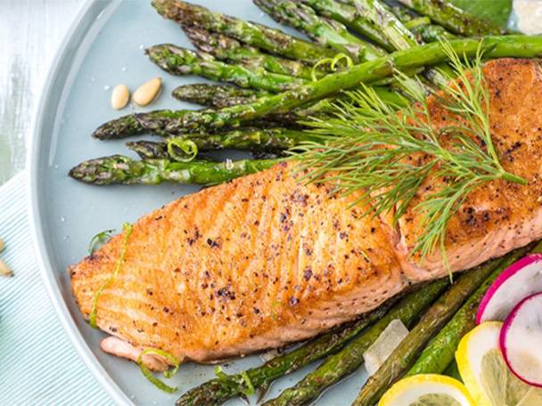 Gebratener Lachs mit Spargel, Dill und Zitronenscheiben auf einem Teller.