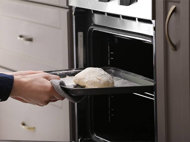 Ein Teigling wird vorsichtig auf ein Backblech in einen Backofen geschoben.