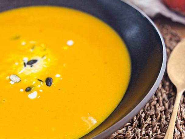 Eine Schale mit goldgelber Kürbiscremesuppe, garniert mit Kernen und Sahne.