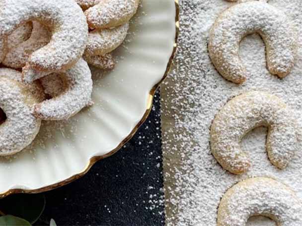 Zuckerbestäubte Vanillekipferl auf einem weißen Teller und einem Backblech.