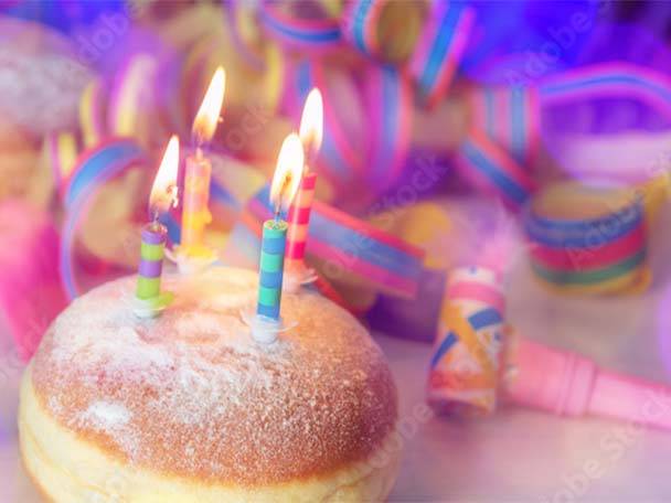 Geburtstags-Donut mit brennenden Kerzen und Partydekoration.