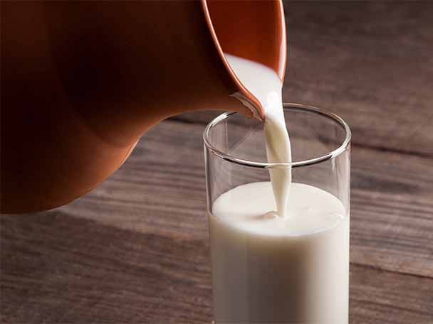 Milch wird aus einem Krug in ein Glas auf einem Holztisch gegossen.