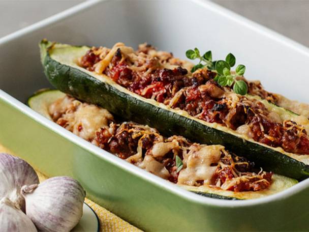 Gefüllte Zucchinihälften mit Hackfleisch, Käse und Kräutern in einer Auflaufform.