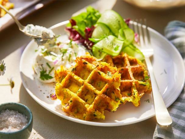 Herzhafte Waffeln mit Salat und Dip auf einem weißen Teller.