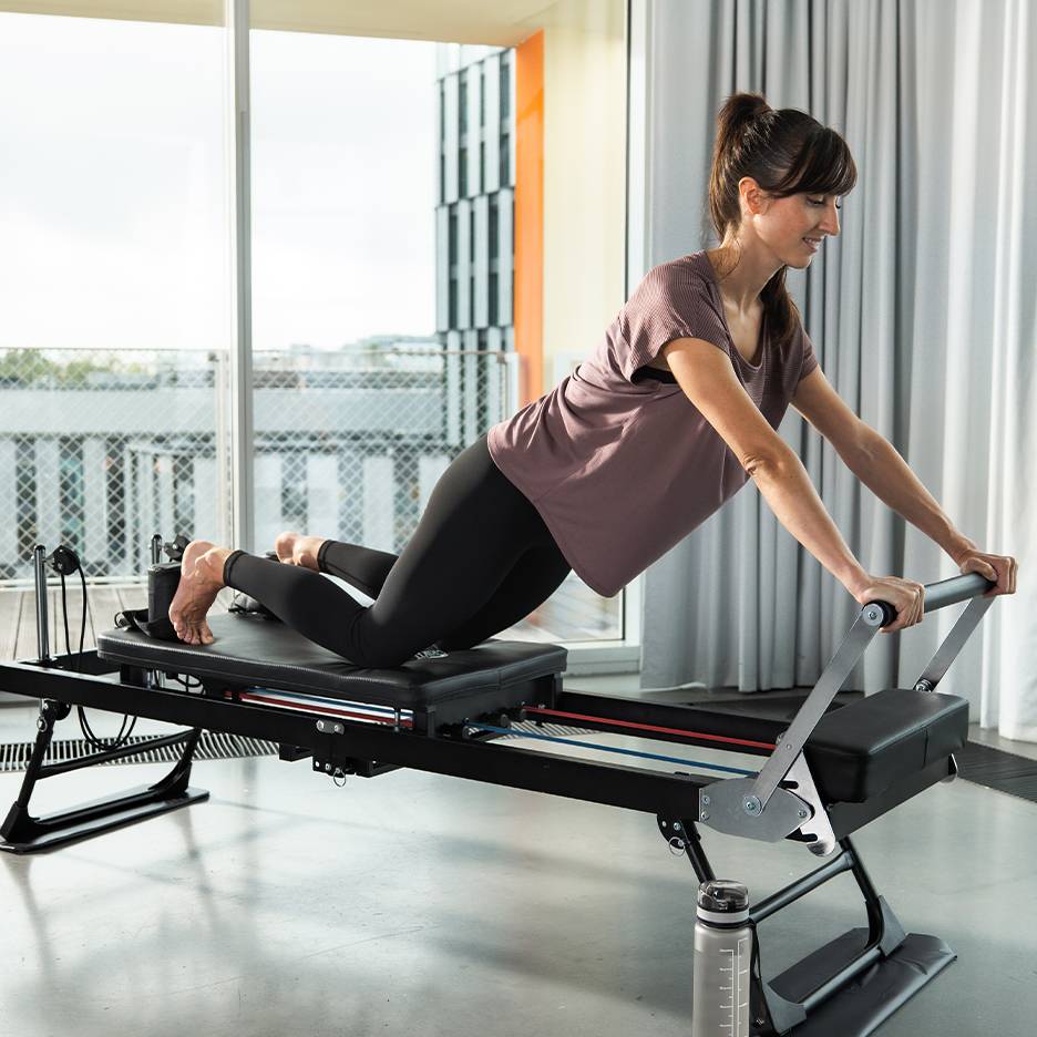 Frau macht Pilates auf einem Reformer mit Federn und Gurten.