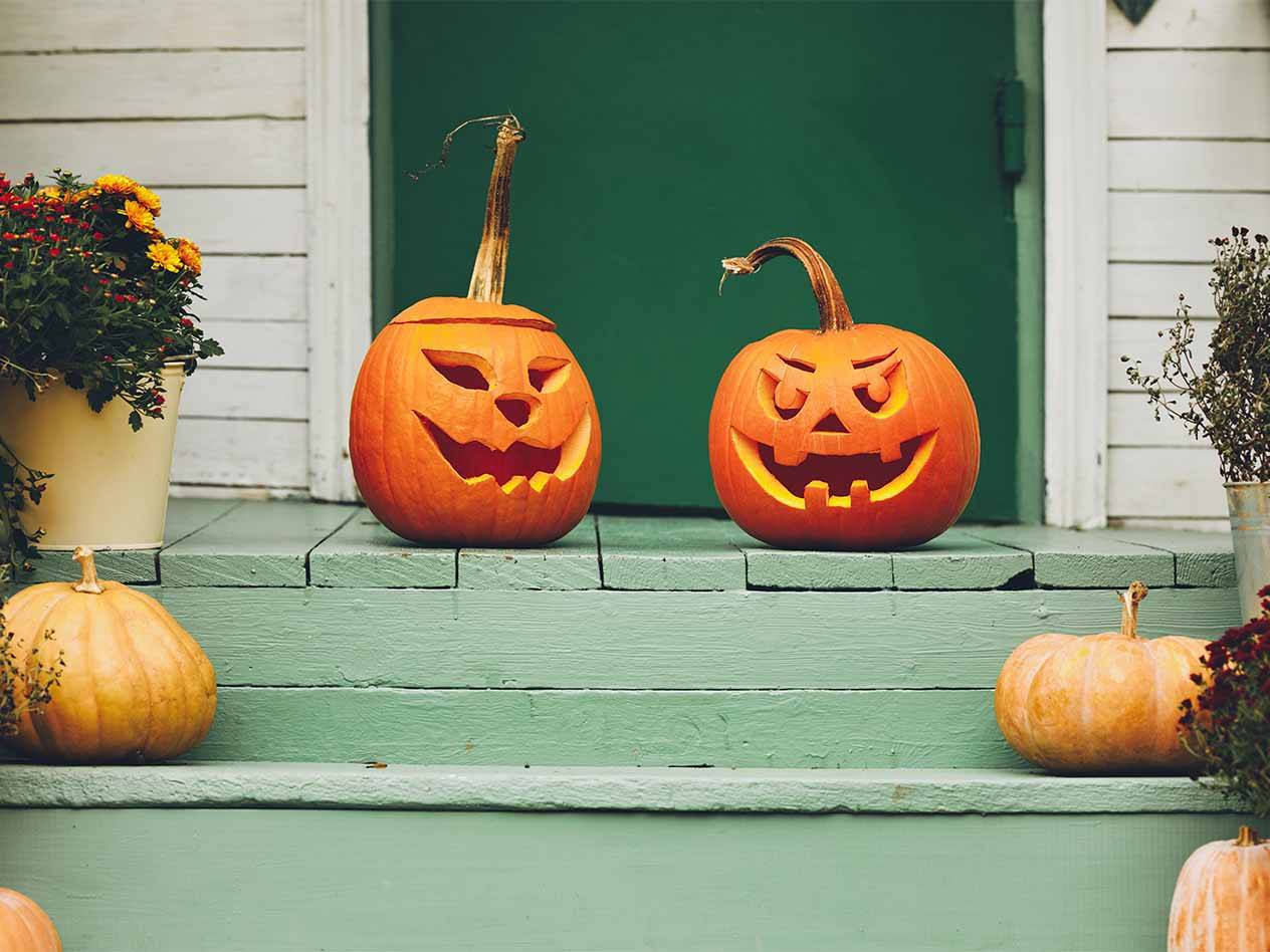 Zwei leuchtende Kürbisse mit geschnitzten Gesichtern auf einer Veranda mit grünen Stufen.