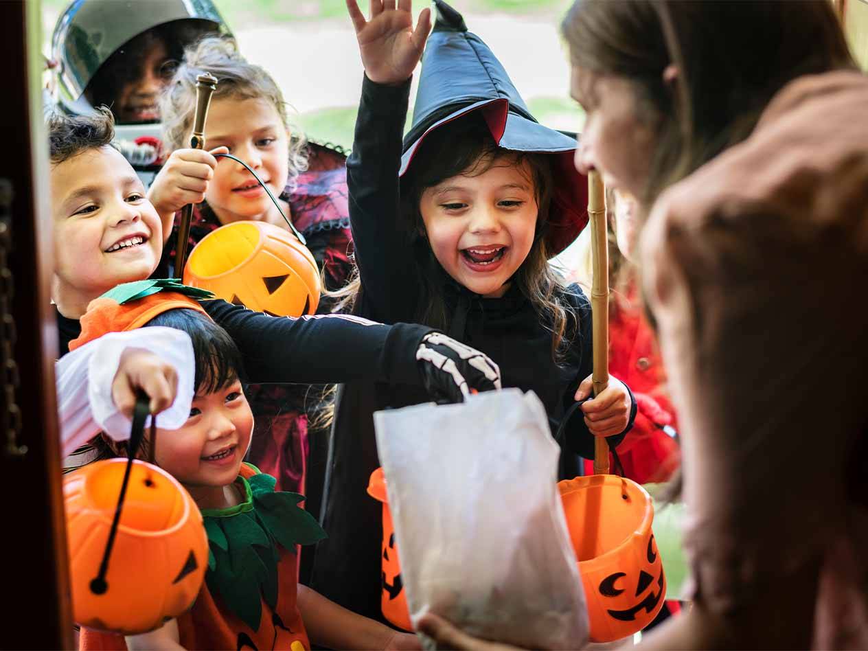 Kinder in Halloween-Kostümen sammeln Süßigkeiten in Kürbiseimern.