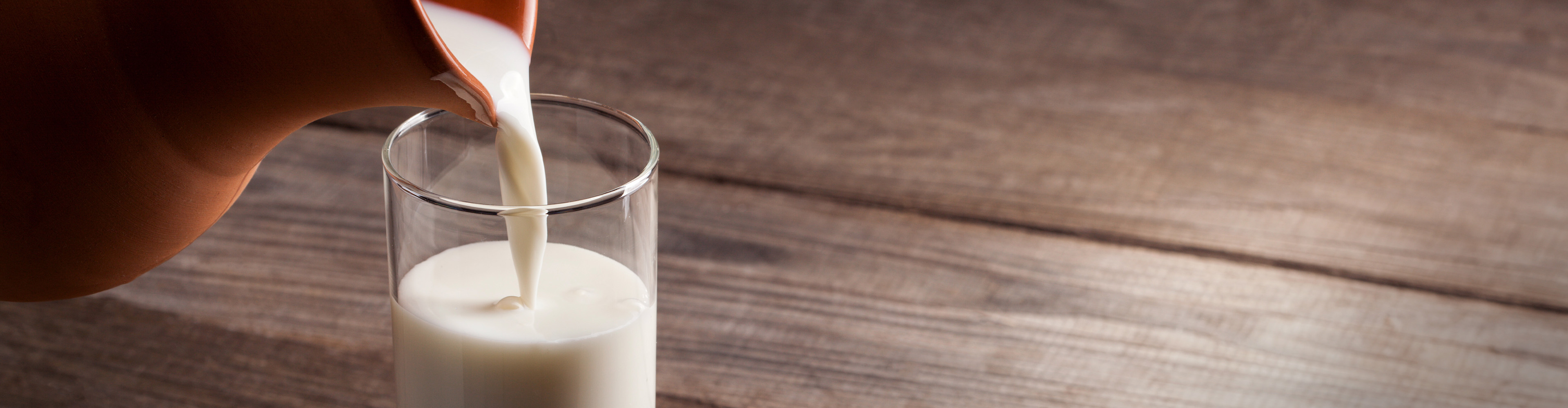 Milch wird aus einem Tonkrug in ein Glas gegossen.