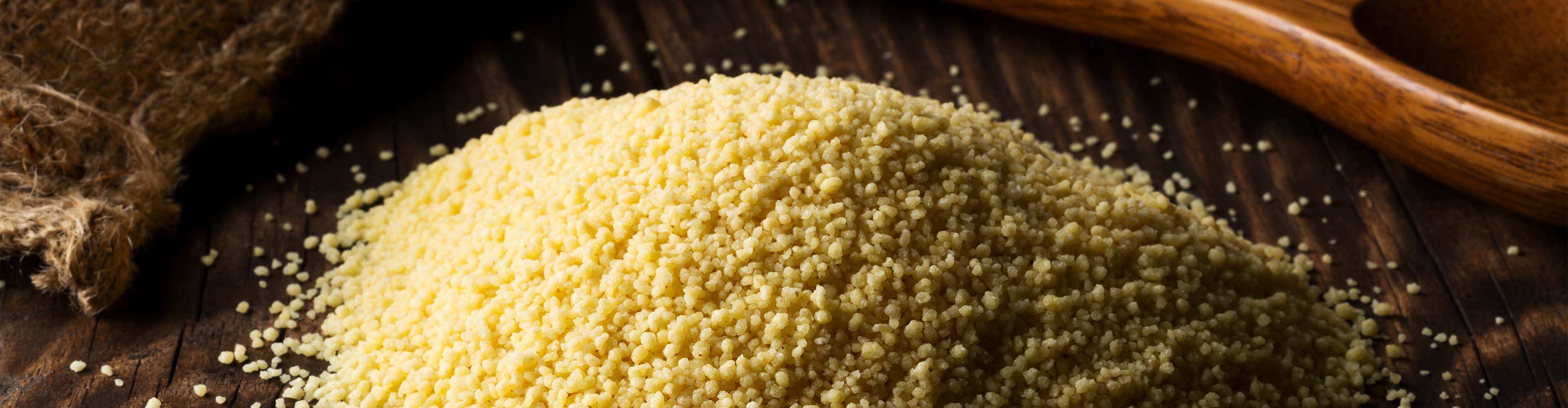 Haufen Couscous auf einem Holztisch mit einem Sack und einem Holzlöffel.