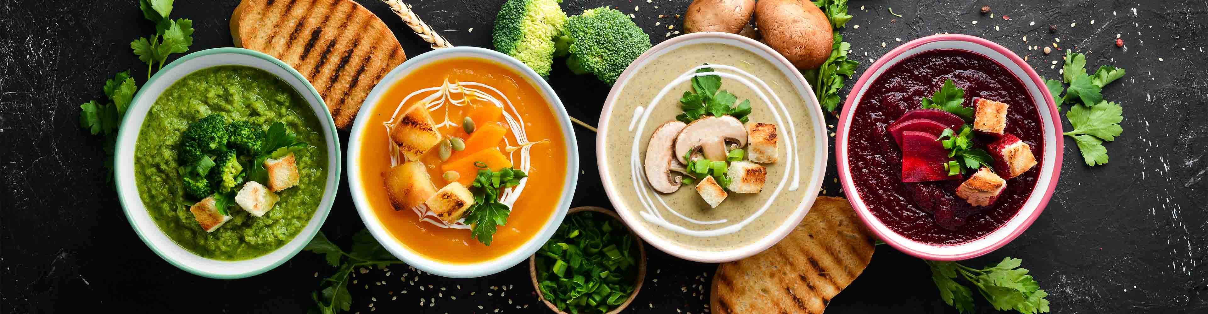 Vier Schalen mit verschiedenen Cremesuppen: Brokkoli, Kürbis, Pilz und Rote Bete.