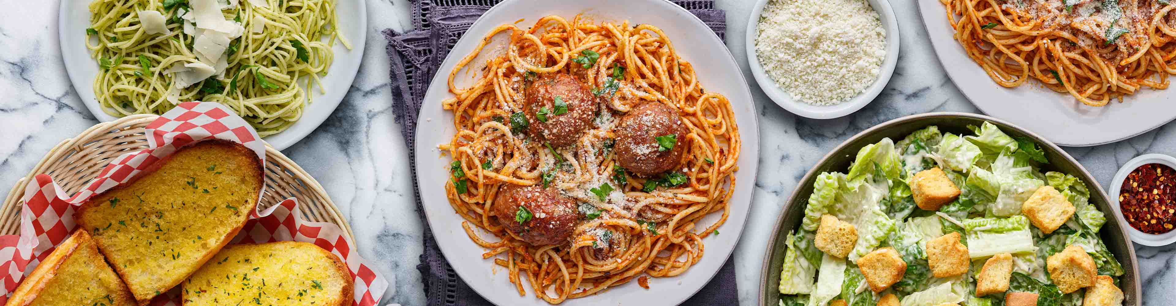 Eine Auswahl an italienischen Gerichten, darunter Spaghetti mit Fleischbällchen, Pesto-Nudeln, Caesar-Salat und Knoblauchbrot.