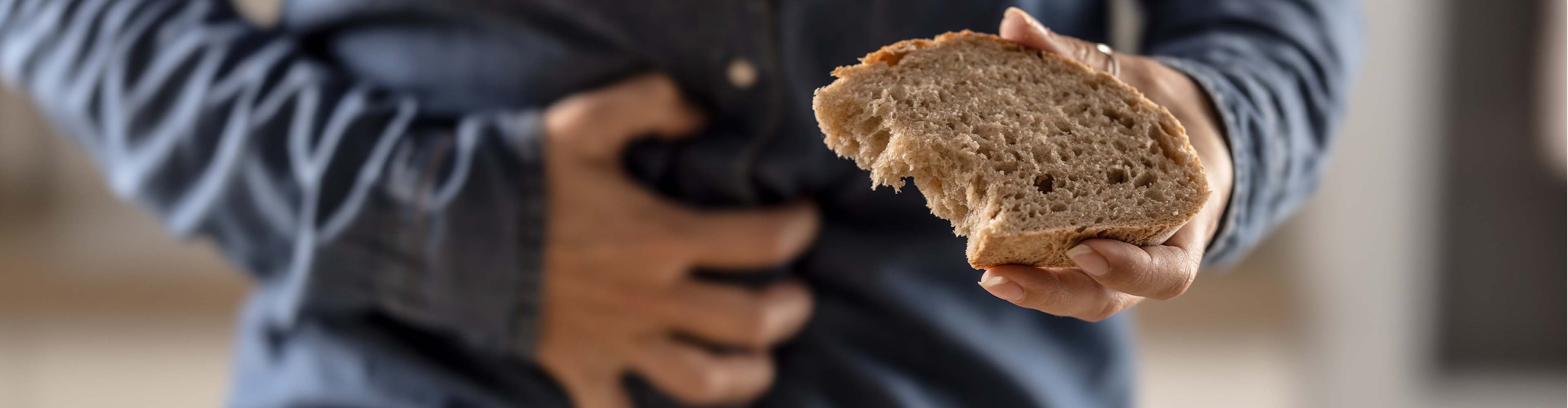 Eine Person hält ein Stück Brot und greift sich an den Bauch, was auf Magenprobleme hindeutet.