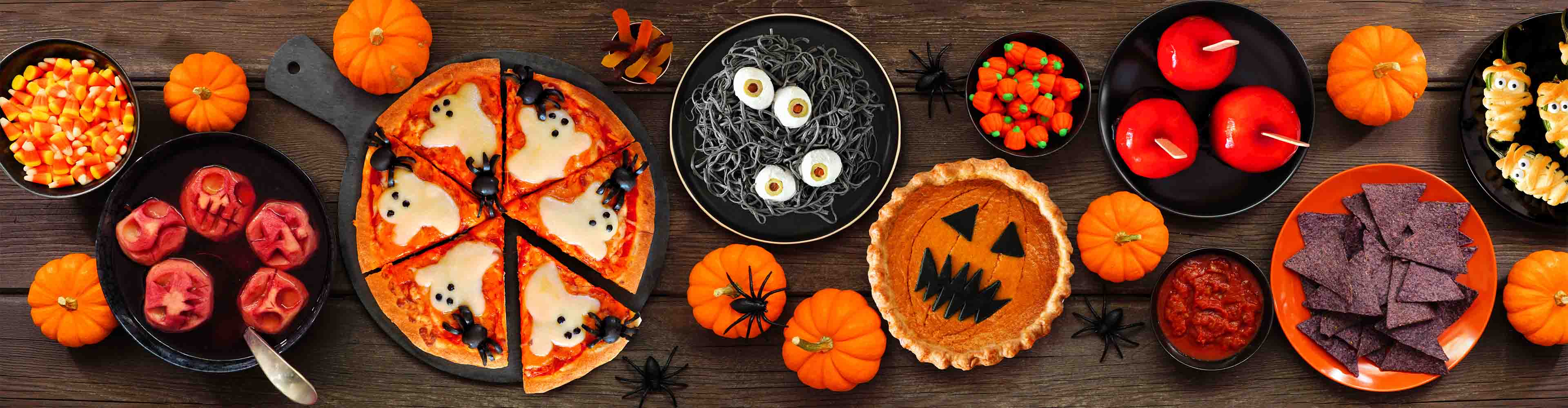 Halloween-Essen und Süßigkeiten, darunter Pizza, Kuchen, Äpfel und Süßigkeiten.