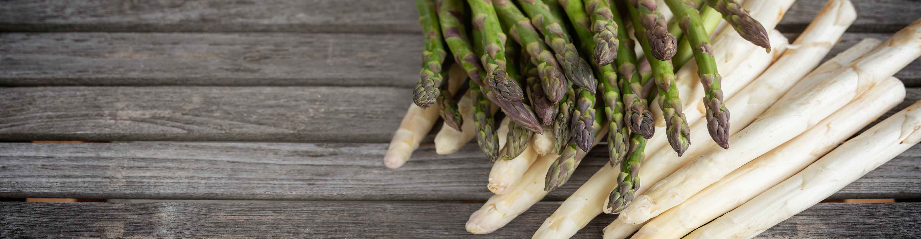 Grüner und weißer Spargel auf einem Holztisch.