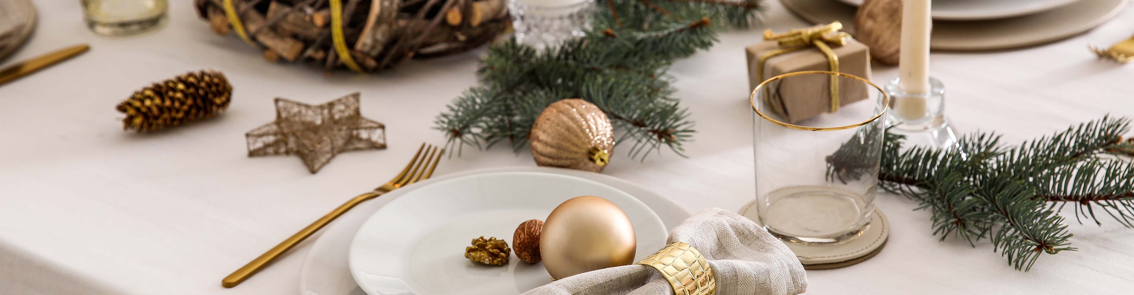 Festlich gedeckter Tisch mit goldenen Dekorationen, Tannenzweigen und Kerzen.