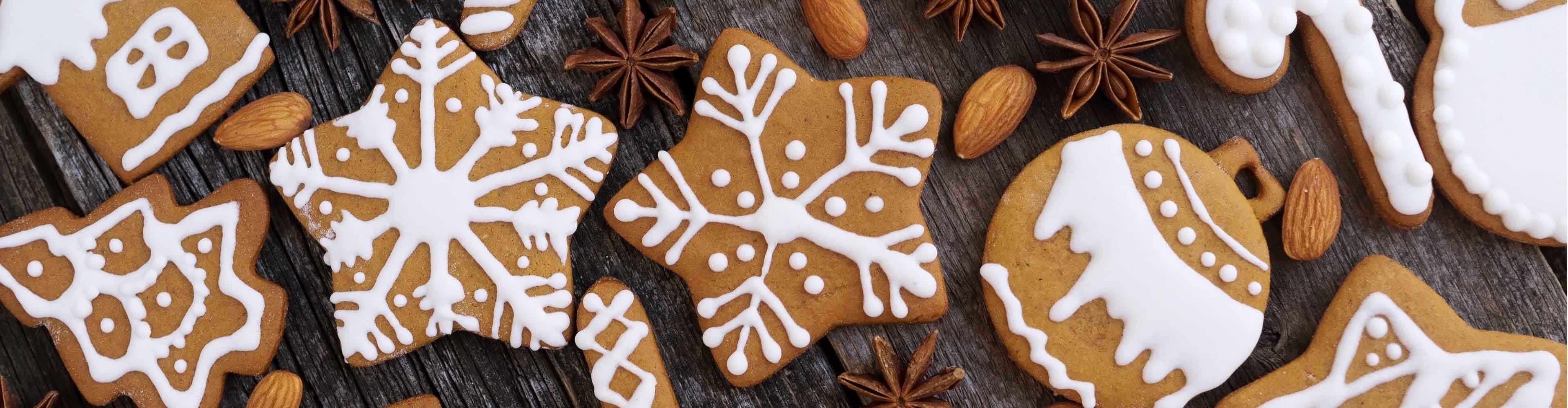 Lebkuchenplätzchen mit weißem Zuckerguss, Mandeln und Sternanis auf Holz.