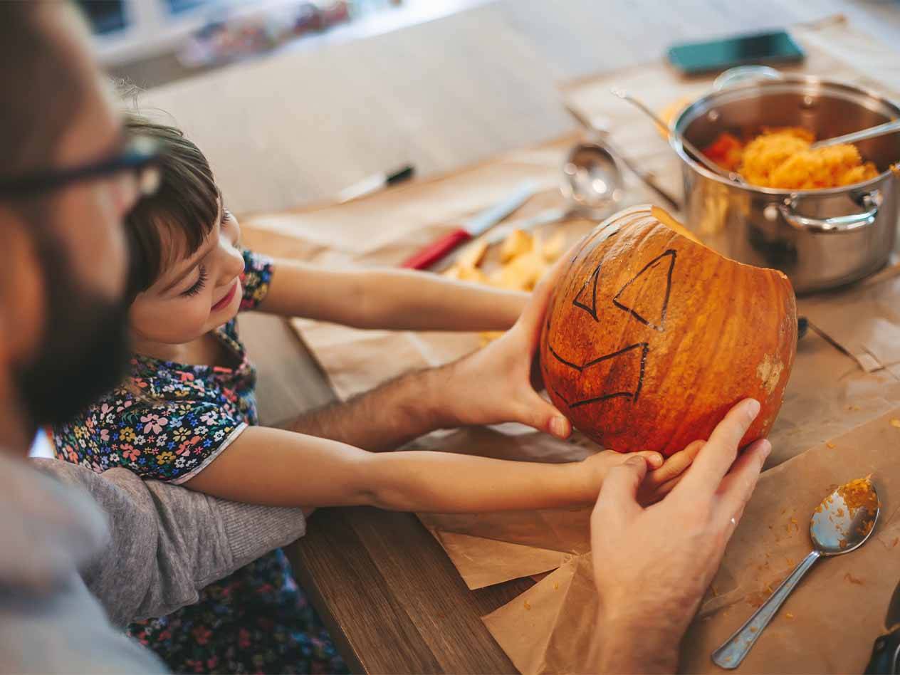 Ein Vater und ein Kind schnitzen einen Kürbis für Halloween.