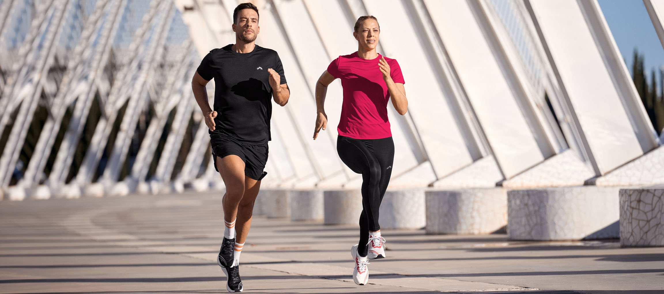 Mann und Frau laufen in Sportkleidung, schwarzen und pinken Oberteilen, schwarzen Shorts und Leggings.
