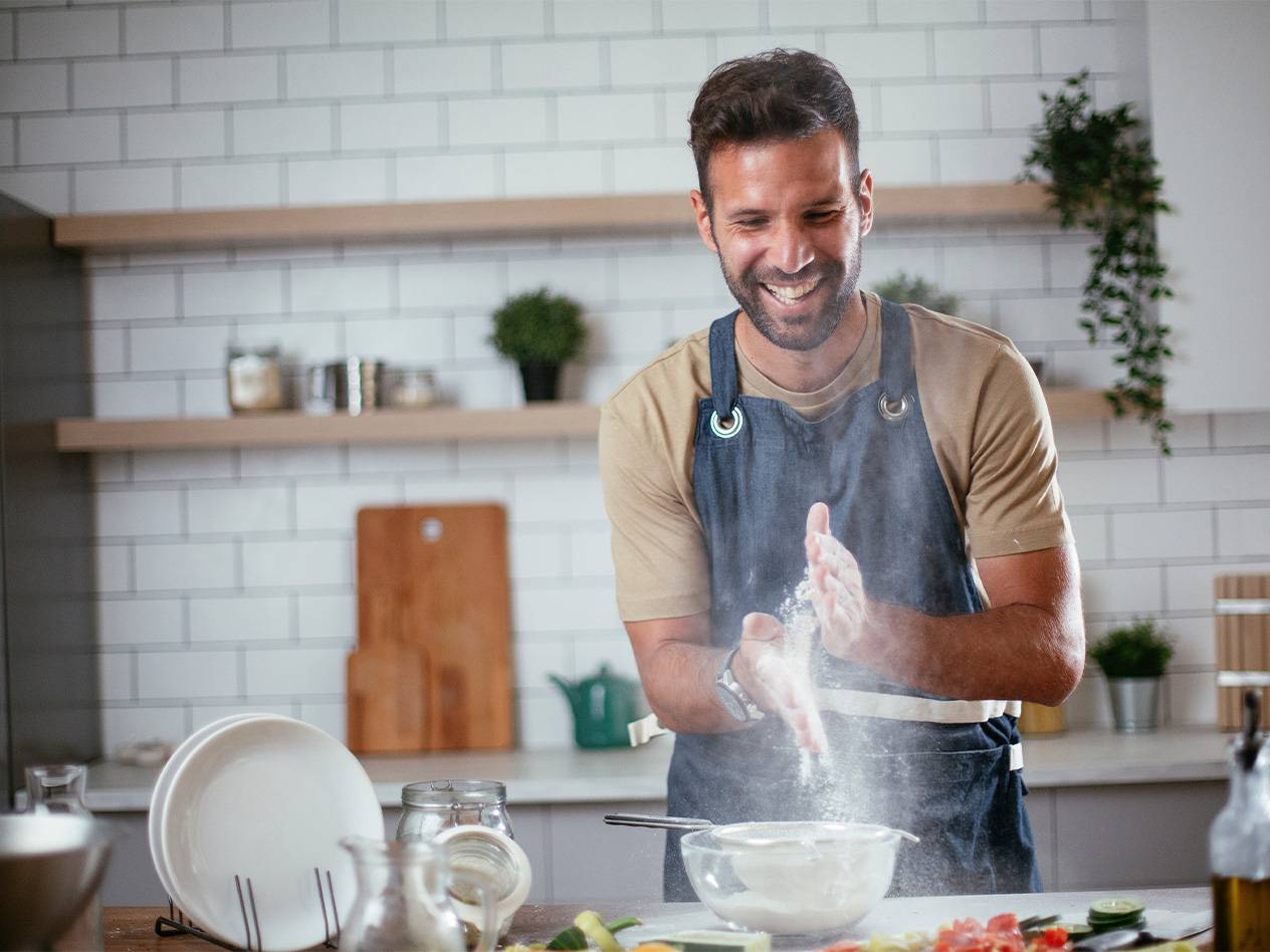 Ein Mann in einer Schürze wirft Mehl in die Luft, während er in der Küche kocht.